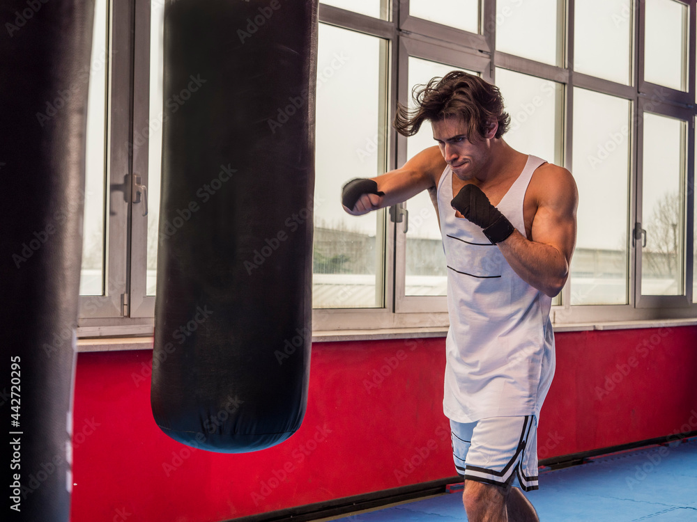 Muscular sportive man training with punching bag while boxing