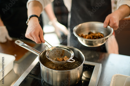 male chef's hand pulls nuts from a boiling pot using a sieve