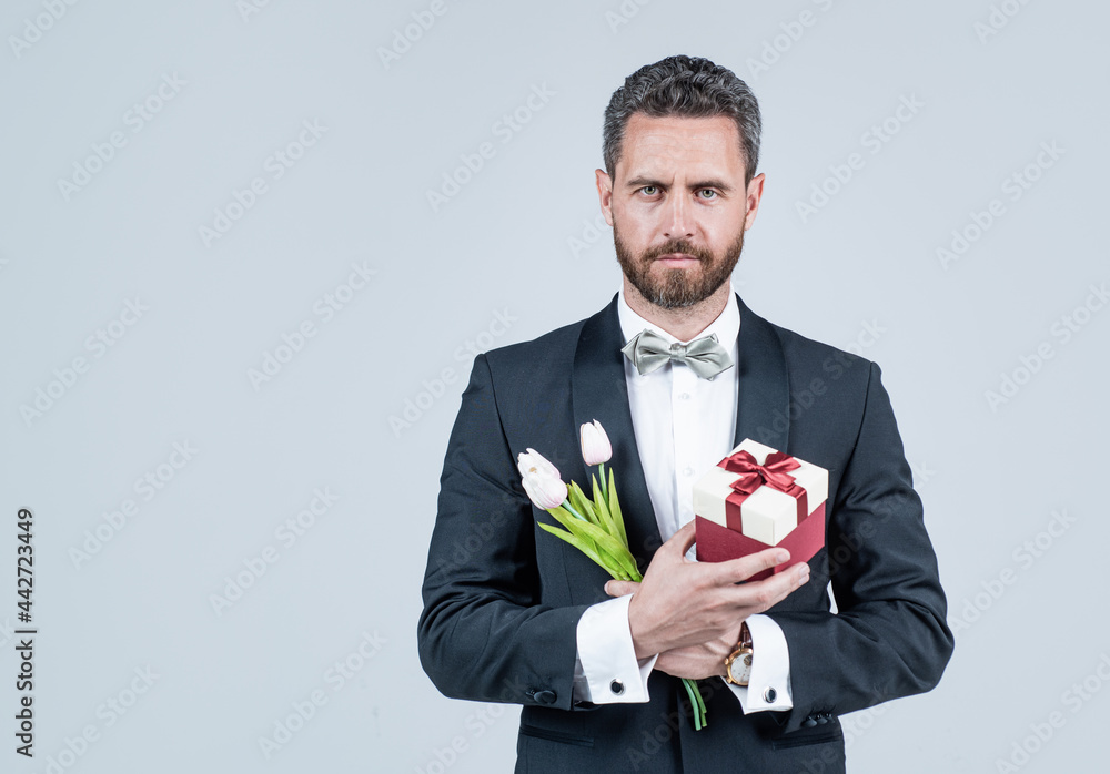 Elegant tuxedo man hold present box and tulips. Spring flowers. Floral shop. Gift store. Elegant tuxedo man hold present box and tulips. Spring flowers. Floral shop. Gift store.