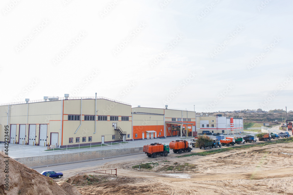 Fototapeta premium Queue with garbage trucks and tractors near warehouse of waste.