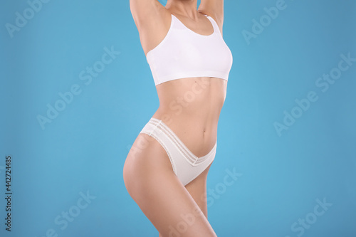 Closeup view of slim woman in underwear on light blue background. Cellulite problem concept © New Africa