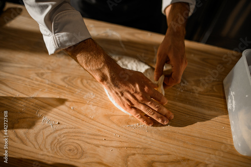 view of male chef's hands who skillfully adjusts the dough on on wooden table.