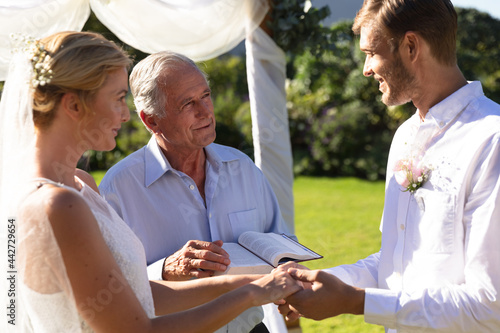 Happy caucasian bride and groom getting married holding hands vowing photo