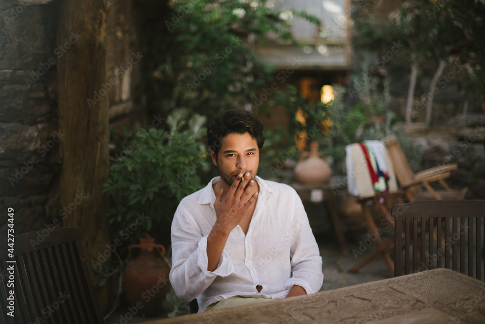 Young dark haired boy smoking a cigar while sitting on a patio Young dark haired boy smoking a cigar while sitting on a patio