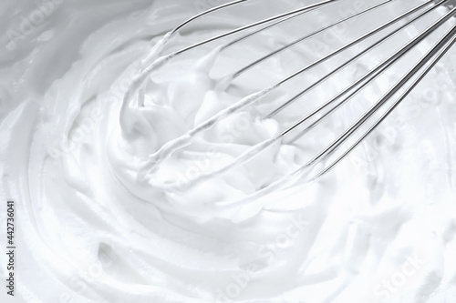 Whipping white cream with balloon whisk, closeup view