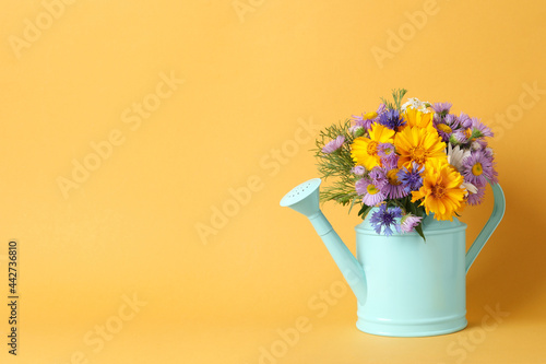 Fototapeta Naklejka Na Ścianę i Meble -  Light blue watering can with beautiful flowers on yellow background, space for text