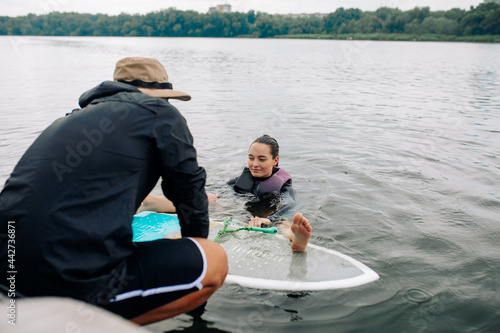 Young woman learns how to stand up on wakesurf board under guidance of coach.