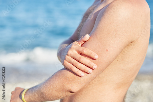 Man uses sun cream for a safe tan with high SPF on the beach. Close up