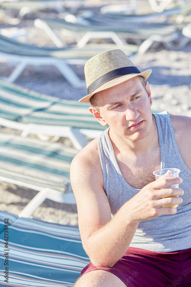 Young caucasian man resting on a lounger with a plastic glass of beer in summer weather. Summer holidays concept