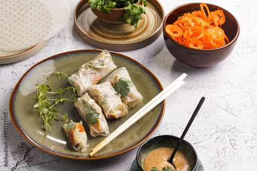 Several spring rolls with chicken, carrot and bamboo sprouts in rice paper on green plate, sesame sauce and coriander on concrete surface photo