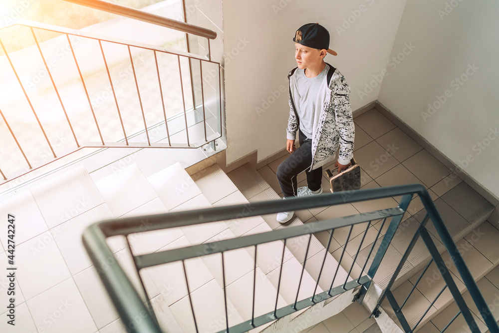 Teenager skateboarder boy with a skateboard going up by staircase home. Youth generation Freetime spending concept image.