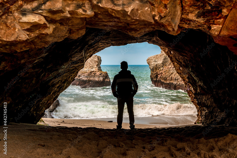 Fototapeta premium The silhouette of a man in a dark cave with a view of the raging ocean and rocks