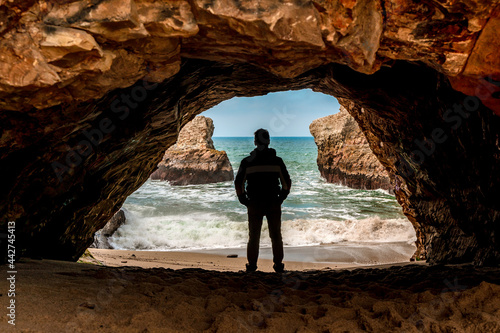 The silhouette of a man in a dark cave with a view of the raging ocean and rocks