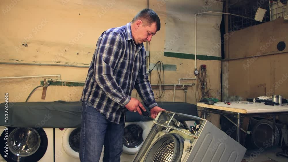 The master attaches a new part to the washing machine with a screwdriver. The man disassembles, assembles, repairs the washing machine. Business concept in the field of maintenance and repair services The master attaches a new part to the washing machine with a screwdriver. The man disassembles, assembles, repairs the washing machine. Business concept in the field of maintenance and repair services