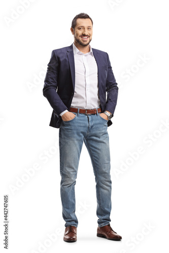 Full length portrait of a man in jeans and suit posing with hands in pockets and smiling