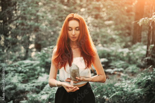 Red-haired beautiful woman holding magic crystal. Meditation Spiritual Forest Background