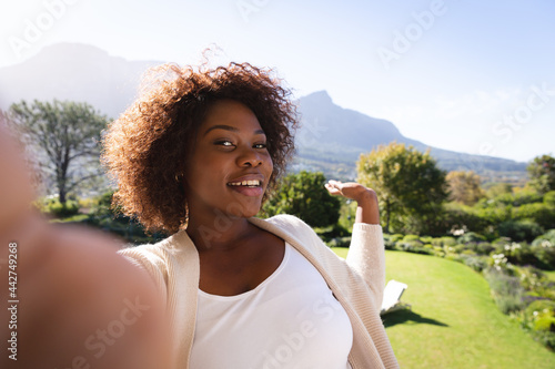 Happy african american woman on sunny balcony of country home making video call, showing view