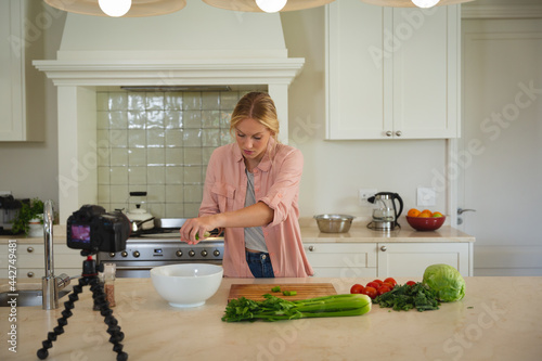 Caucasian woman in kitchen preparing food and using camera, making cooking vlog
