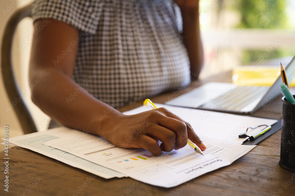 Midsection of african american woman working in living room using laptop and making notes Midsection of african american woman working in living room using laptop and making notes
