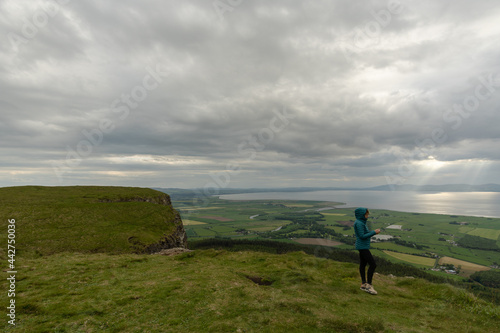 Woman standing on top of mountain looking at her mobile phone, in Binevenagh Northe Ireland
