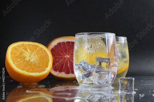 Cooking Lemonade Water in a glass of ice and fruit orange grapefruit on a black background. Summer drinks. A lemonade drink