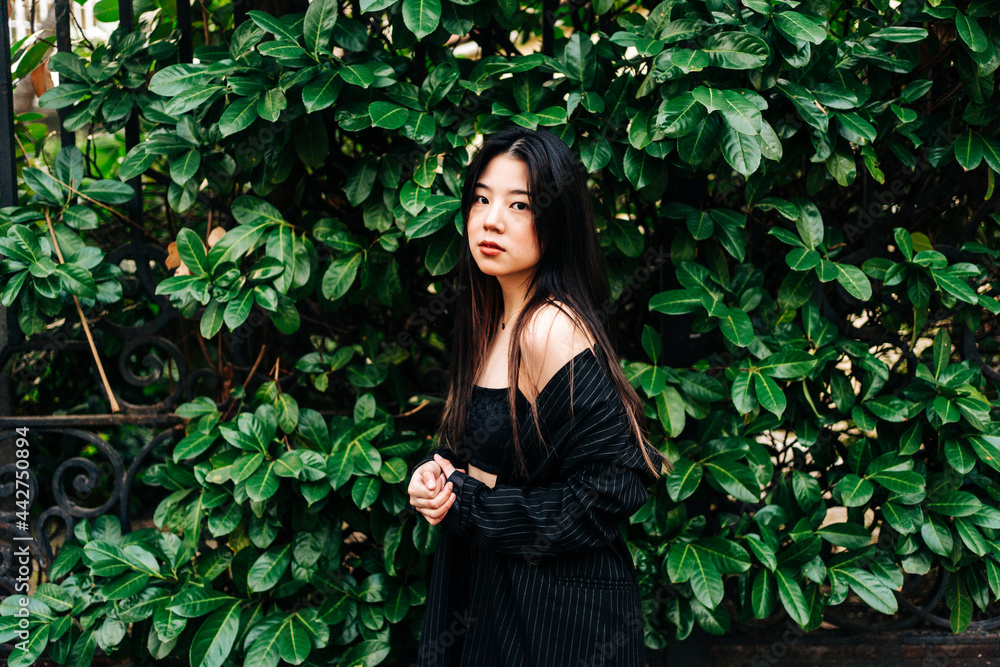 Long hair brunette Asian woman looking at camera with a garden behind her Long hair brunette Asian woman looking at camera with a garden behind her