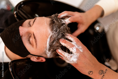 Crop tattooed barber washing hair of client in salon photo
