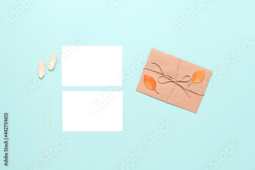 Blank business cards mockup, letter, autumn leaves and dry grass on pastel mint blue paper background. Autumn stationery still life. Top view, flat lay.