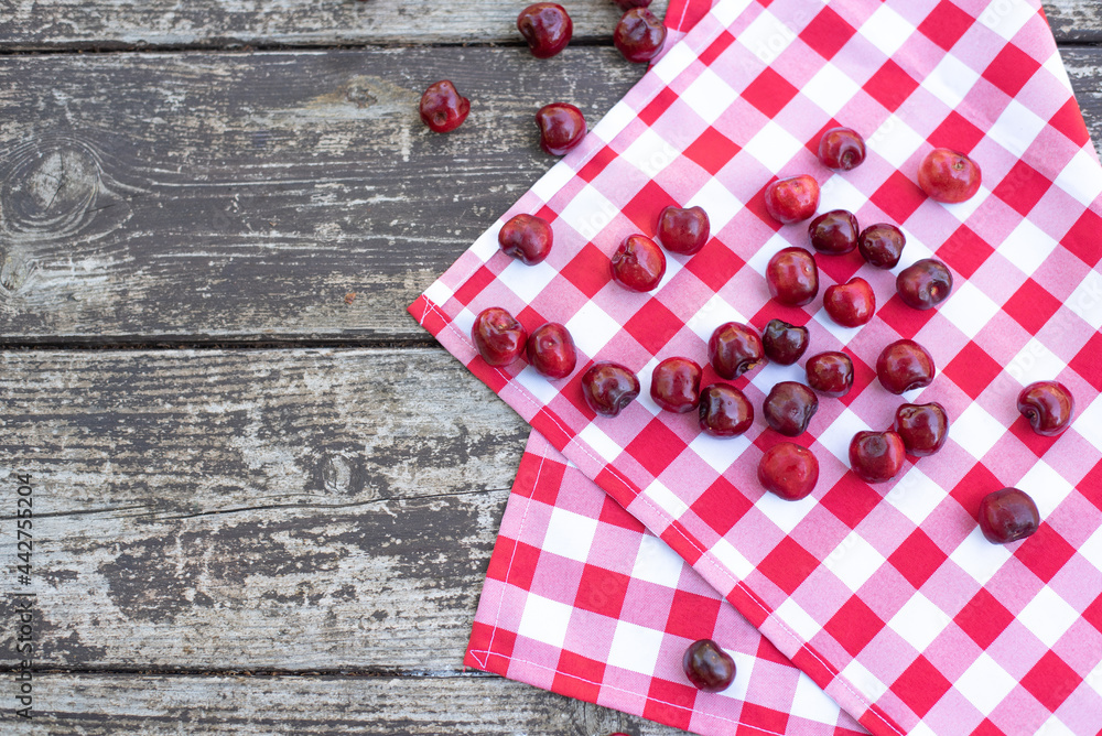 Obraz premium Red fresh cherries on wooden table with cell white red napkin top view, space for text. Ripe berries are delicious and contain healthy vitamins. Tasty Italy desert is obtained from fresh fruits