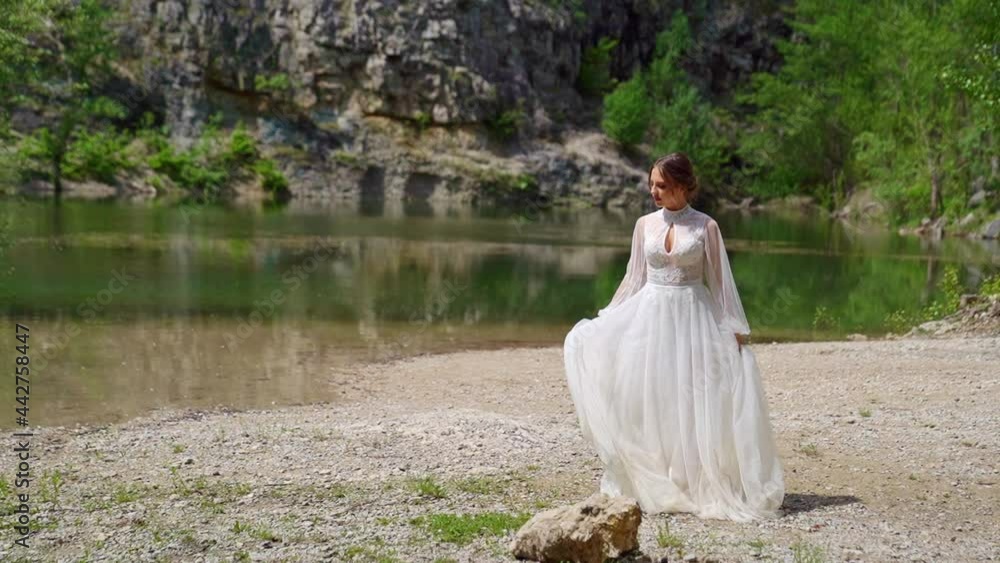 The bride in a white wedding dress walks along the bank of a mountain river. The bride in a white wedding dress walks along the bank of a mountain river.