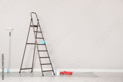 Decorator's tools and ladder near white wall indoors, space for text