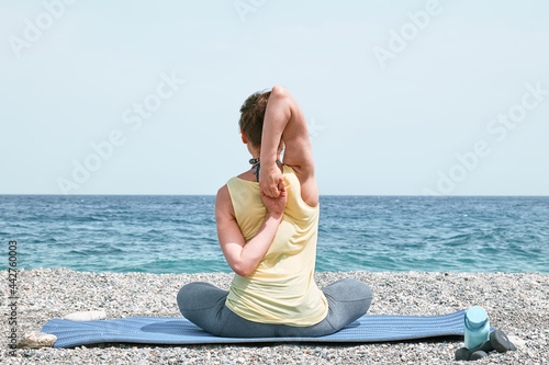 Slim Woman doing Gomukhasana or Cow Face Pose on the beach in the morning. Strengthening muscles of legs and coordination of body. Practicing yoga outdoors