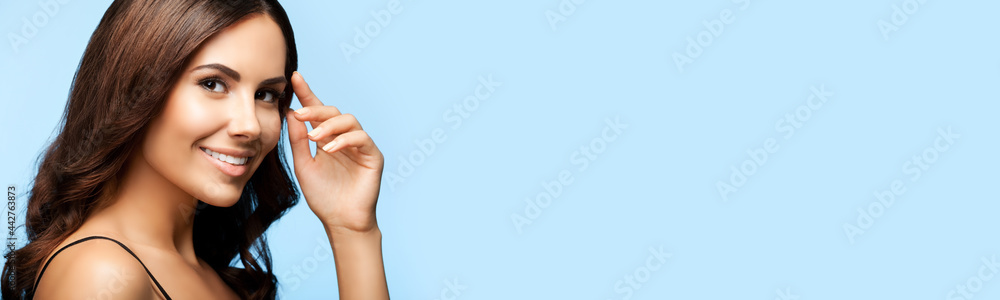 Obraz premium Portrait of happy smiling beautiful woman in black casual tank top, over bright blue background. Brunette girl at studio. Beauty concept. Wide horizontal composition image with copy space.