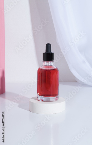 Glass dropper bottle with pipette with red cosmetic liquid or oil on podium