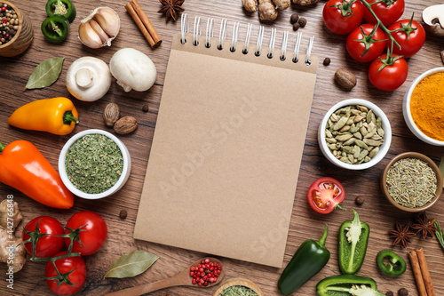 Open recipe book and different ingredients on wooden table, flat lay. Space for text photo