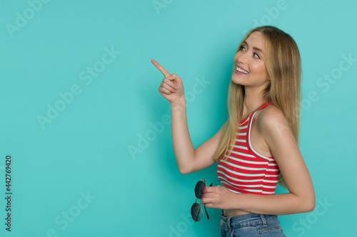 Happy Young Woman In Striped Tank Top Is Holding Sunglasses And Pointing