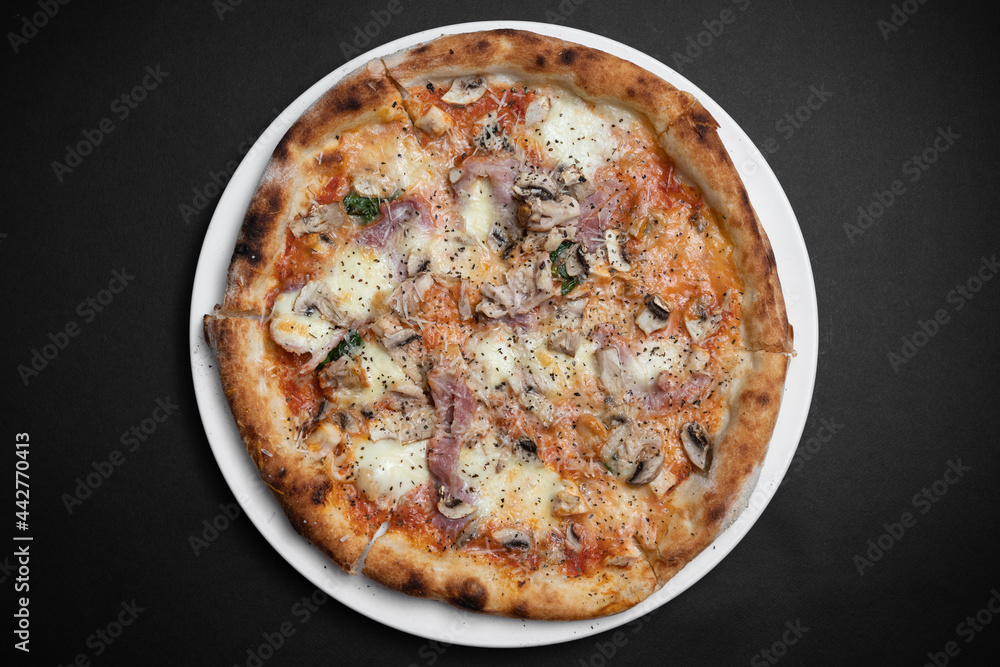 top view of italian pizza with ham, mushrooms and cheese on black background top view of italian pizza with ham, mushrooms and cheese on black background