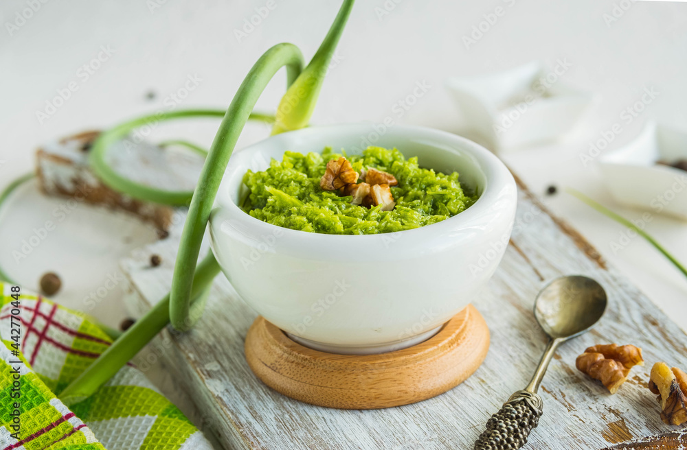 Garlic arrow pesto sauce with walnuts in a white mortar on a light concrete background. Sauce recipes. Garlic arrow pesto sauce with walnuts in a white mortar on a light concrete background. Sauce recipes.