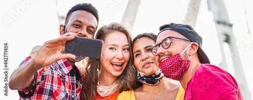 Multiracial friends taking selfie with face mask in coronavirus time - Young people having fun in holiday - new lifestyle concept