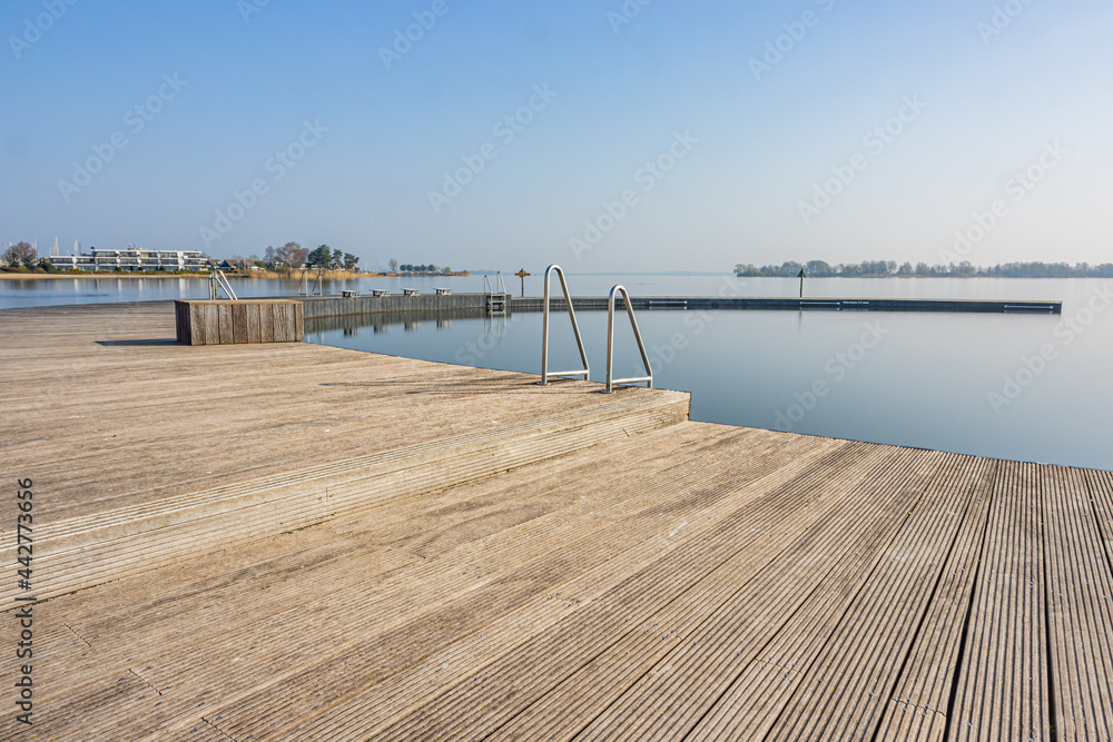 Wooden platform or atoll with metal stairs in natural swimming pool at Woldstrand Zeewolde beach recreation area, spring day with light fog in Flevoland, Netherlands