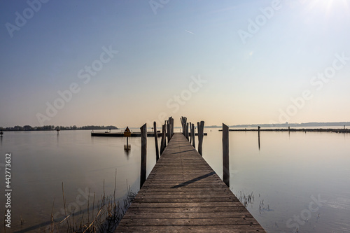 Straight wooden bridge between calm waters towards the recreation area in the Atoll at Woldstrand Zeewolde beach, sunset on a spring day in Flevoland, Netherlands
