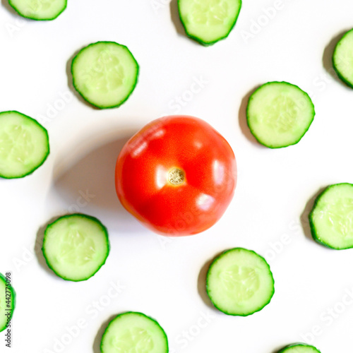 repeating pattern of sliced semicircles of fresh raw vegetable cucumbers for salad and a whole tomato in the center isolated on a white background flat lay, top view. square