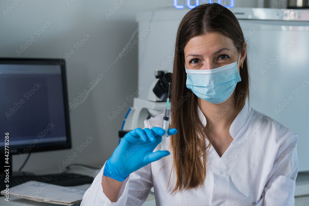 Female doctor with medical mask and gloves prepares prefilled syringe for injection by removing cap Female doctor with medical mask and gloves prepares prefilled syringe for injection by removing cap