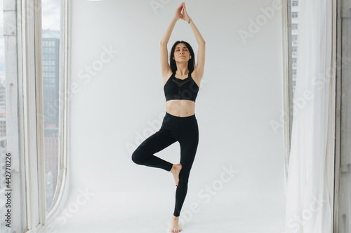 armenian woman in black sportswear practicing tree pose with raised hands