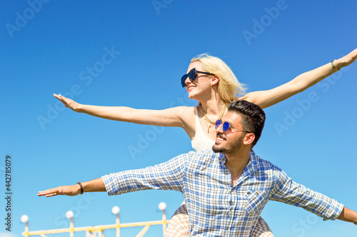 Happy couple piggyback together with arms outstretched on a sunny day.