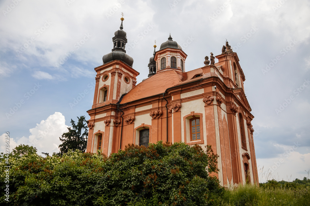 Valec, Western Bohemia, Czech Republic, 19 June 2021:  Baroque red and yellow church of the Holy Trinity with towers near castle at summer day