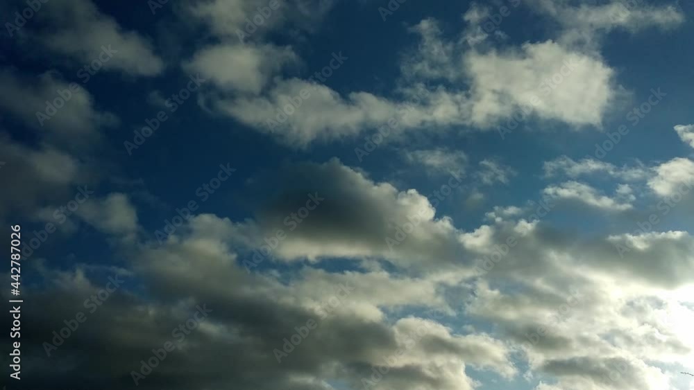 Low angle view time-lapse of white and grey clouds passing by in the dark blue sky with light from the side. Nature motion background with clouds moving fast Low angle view time-lapse of white and grey clouds passing by in the dark blue sky with light from the side. Nature motion background with clouds moving fast