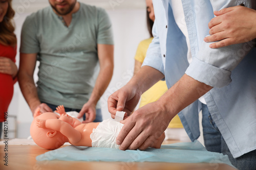 Future fathers and pregnant women learning how to swaddle baby at courses for expectant parents indoors, closeup photo