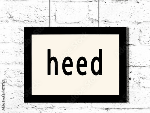 Black frame hanging on white brick wall with inscription heed