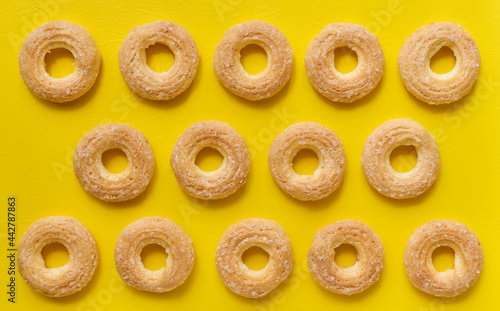 Rows of custard cookie rings on yellow background, top view, flat lay